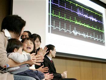 「笑い測定機」の画面と、実験に参加して笑顔を見せる家族=20日、関西大